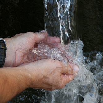 Hands under a gushing water spring